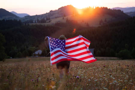 Young woman holding american USA flag in the sunset. Independence Day or traveling in America concept.の写真素材