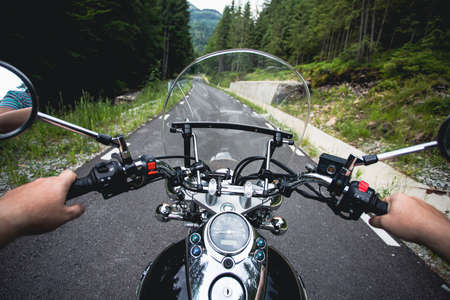 Close-up on the hands of a motorcycle driver riding on forest road. Travel and sport, speed and freedom conceptの写真素材