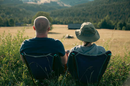 Couple in summer meadow looking at magic sunset over hills. Relaxation, nature and tourism concept.の写真素材