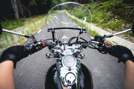 Close-up on the hands of a motorcycle driver riding on forest road. Travel and sport, speed and freedom conceptの写真素材