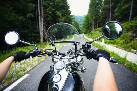 Close-up on the hands of a motorcycle driver riding on forest road. Travel and sport, speed and freedom conceptの写真素材
