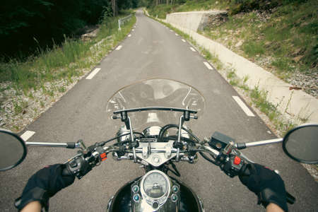Close-up on the hands of a motorcycle driver riding on forest road. Travel and sport, speed and freedom conceptの写真素材