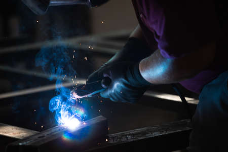 Handyman performing welding and grinding at his workplace in the workshop, while the sparks "fly" all around him. He is wearing a protective helmet and equipment.の写真素材