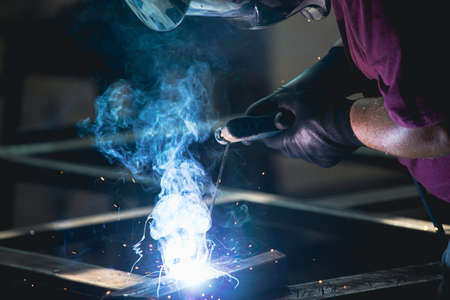 Handyman performing welding and grinding at his workplace in the workshop, while the sparks "fly" all around him. He is wearing a protective helmet and equipment.の写真素材