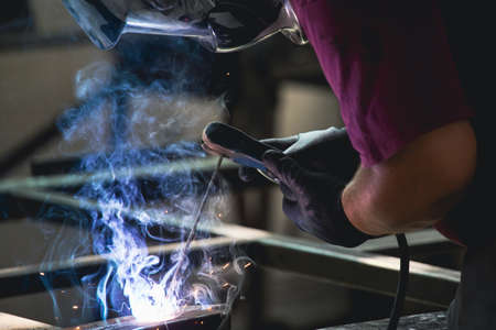 Handyman performing welding and grinding at his workplace in the workshop, while the sparks "fly" all around him. He is wearing a protective helmet and equipment.の写真素材