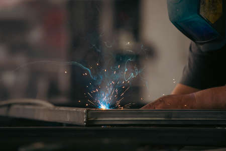 Handyman performing welding and grinding at his workplace in the workshop, while the sparks "fly" all around him. He is wearing a protective helmet and equipment.の写真素材