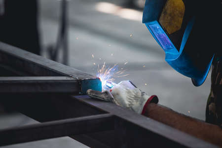 Handyman performing welding and grinding at his workplace in the workshop, while the sparks "fly" all around him. He is wearing a protective helmet and equipment.の写真素材