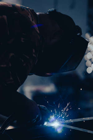 Handyman performing welding and grinding at his workplace in the workshop, while the sparks "fly" all around him. He is wearing a protective helmet and equipment.の写真素材