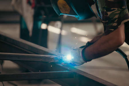 Handyman performing welding and grinding at his workplace in the workshop, while the sparks "fly" all around him. He is wearing a protective helmet and equipment.の写真素材