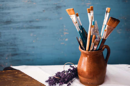 Still life of paint brushes  in clay jug an lavender flower on vintage turquoise backgroundの写真素材