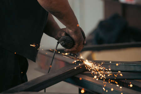 Profesional fabric worker cutting metal profile on the work table with an electric grinder in the industrial workshop.の写真素材