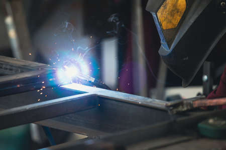 Handyman performing welding and grinding at his workplace in the workshop, while the sparks "fly" all around him. He is wearing a protective helmet and equipment.の写真素材