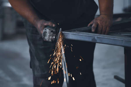 Profesional fabric worker cutting metal profile on the work table with an electric grinder in the industrial workshop.の写真素材