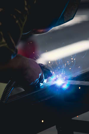 Handyman performing welding and grinding at his workplace in the workshop, while the sparks "fly" all around him. He is wearing a protective helmet and equipment.の写真素材