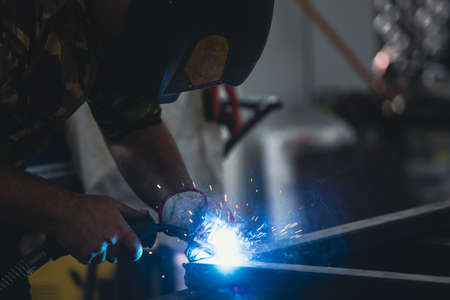 Handyman performing welding and grinding at his workplace in the workshop, while the sparks fly all...