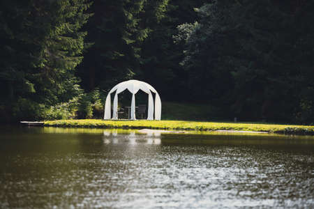 White wedding pavilion altar next to a small lakeの写真素材
