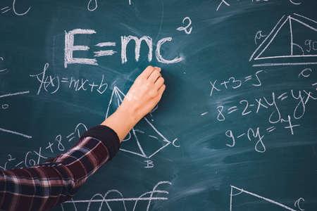 Close-up shot of a hand holding chalk and writing mathematical equations on the blackboard. Education concept.の写真素材