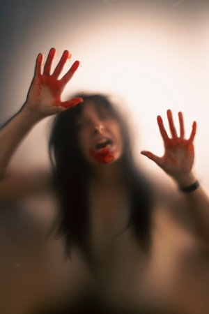 Horror ghost woman with blooded hands behind the matte glass. Halloween festival concept.の写真素材