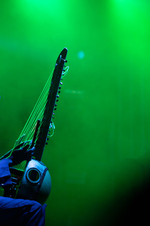 Artist performing traditional wooden harp, kora during event, in colorful stage lights.