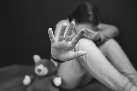Child violence and abused concept. Little girl sitting in a dark room, showing stop sign