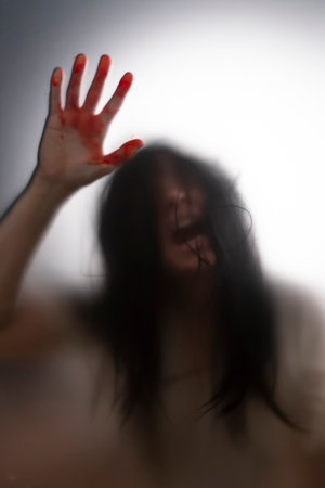 Horror ghost woman with blooded hands behind the matte glass. Halloween festival concept.の写真素材