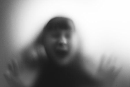 Scared, screaming girl behind the matte glass. Halloween festival concept.の写真素材