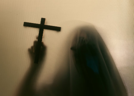 Horror ghost woman holding a cross behind the matte glass. Halloween festival concept.の写真素材