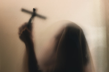 Horror ghost woman holding a cross behind the matte glass. Halloween festival concept.の写真素材