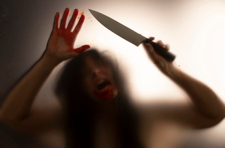 Horror, halloween background - Shadowy figure behind glass holding a knife and with blooded handsの写真素材