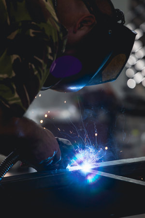 Handyman performing welding and grinding at his workplace in the workshop, while the sparks "fly" all around him. He is wearing a protective helmet and equipment.の写真素材