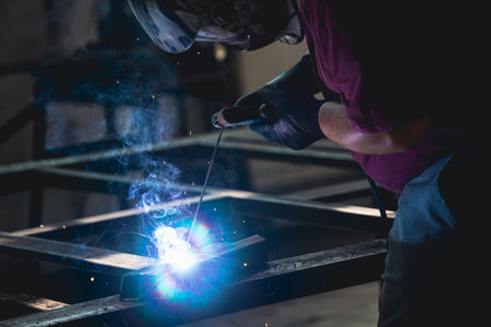 Handyman performing welding and grinding at his workplace in the workshop, while the sparks "fly" all around him. He is wearing a protective helmet and equipment.の写真素材