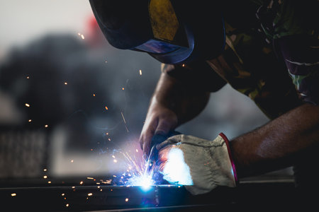 Handyman performing welding and grinding at his workplace in the workshop, while the sparks "fly" all around him. He is wearing a protective helmet and equipment.の写真素材