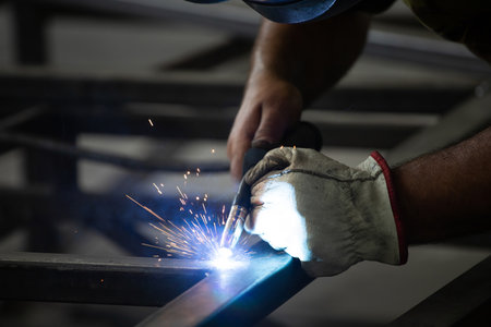 Handyman performing welding and grinding at his workplace in the workshop, while the sparks "fly" all around him. He is wearing a protective helmet and equipment.の写真素材