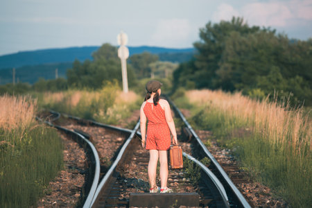 Retro styled photo of little girl with old luggage at the railwaysの写真素材