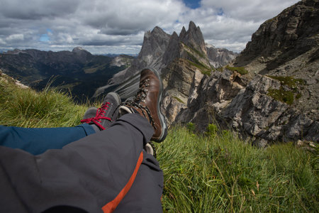 Legs of traveler couple sitting on a high mountain top in Seceda, Dolomite mountains, Italy. Concept...