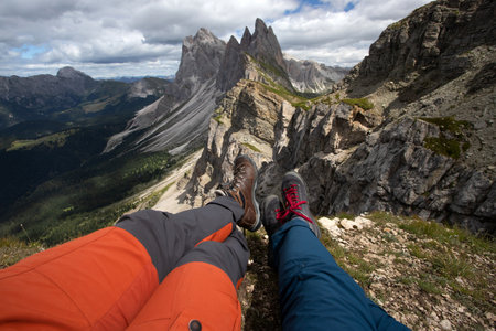 Legs of traveler couple sitting on a high mountain top in Seceda, Dolomite mountains, Italy. Concept of freedom, adventure, summer vacation activityの写真素材