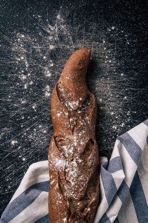 Handmade rye bread wrapped with a cloth over a stone table. Some flour has fallen on the table. Top viewの写真素材