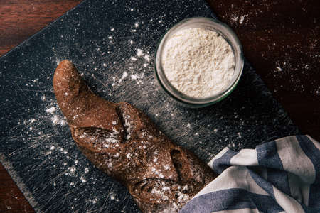 Handmade rye bread wrapped with a cloth over a stone table and a flour jar next to it.