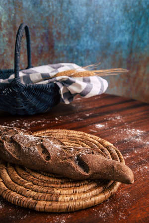 Handmade rye bread over a wooden table with spikes and cloth in a basket and a flour jar.の写真素材