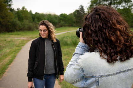 Young white woman taking pictures of her friend in the park with a digital camera.