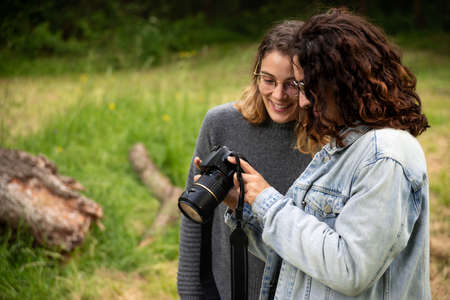 Two young white women in the park joyfully watching the pictures taken on her digital camera.