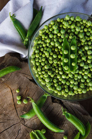 Crystal bowl full of green peas on a wooden table. In the table there are some green peas and a linen cloth. Rustic style. Top view.の写真素材