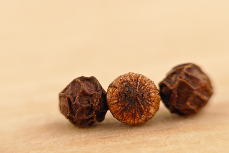 three black pepper seeds (Piper nigrum) on the wooden surfaceの写真素材