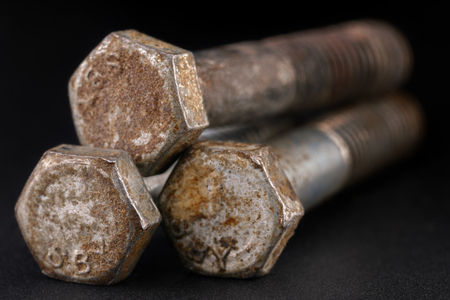 three old dirty and rusty bolts lying on a black surface