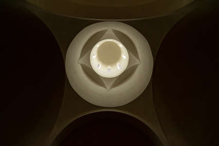 Downside view of a church's dome, lighted through the windows. It has geometrical forms and arcs.