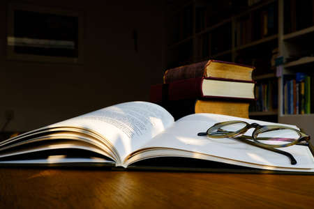 Close up of open text book with eye glasses on wooden desk in library. Old books and bookshelf background. Education concept. Selective focusの写真素材