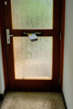 Bennekom, Netherlands,June 30,2020:Dutch newspaper hanging in door mailbox. Old brown door with glass and in door mailbox and doormat. Netherlandsのeditorial素材