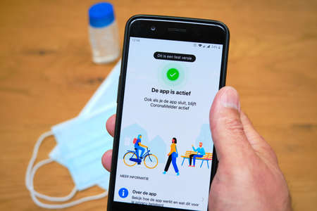 Bennekom,Netherlands,Juli,7,2020:Smartphone with Dutch Corona tracking app named:Coronamelder. Unsharp face mask and disinfectant. Dutch text:This is a test version.App is active even when app closes.のeditorial素材
