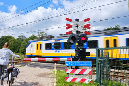 Railway crossing with barriers and blinking red lights and unsharp high speed train. Dutch text,Wait till red light is gone,possibility of other trainの写真素材