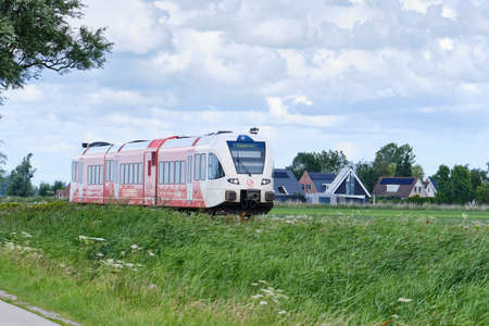 Boazum,Friesland,the Netherlands,July 21,2020:Arriva diesel passenger train to Stavoren through typical Dutch grassland area, Friesland district. Sunny day, blue sky and white clouds, the Netherlands.の写真素材